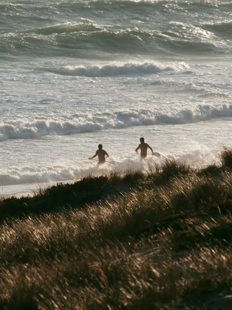 Two people heading into the surf from the dunes