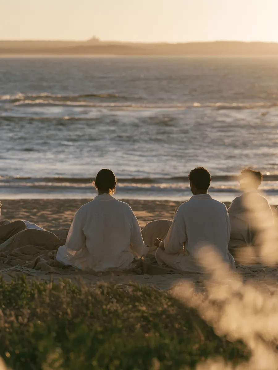 Guests meditating on the beach as the sun sets over the Atlantic